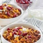 Bowls of homemade Cincinnati chili topped with beans, cheese, and chili.