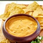 Green chile queso dip on a platter with tortilla chips and fresh cilantro.