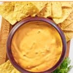 Green chile queso dip in a wood bowl served with tortilla chips.