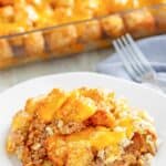 A serving of ground beef and tater tot casserole on a plate in front of the casserole.