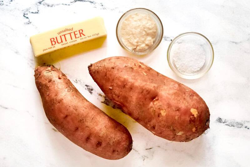 two large sweet potatoes, a stick of butter, horseradish sauce, and salt arranged on a marble surface.