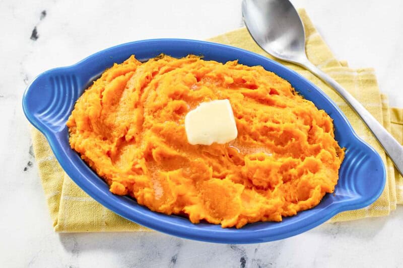 vibrant orange mashed sweet potatoes topped with melting butter, sitting next to a silver serving spoon.
