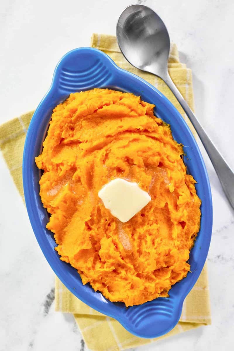 horseradish mashed sweet potatoes in a blue serving boat, garnished with a pat of butter