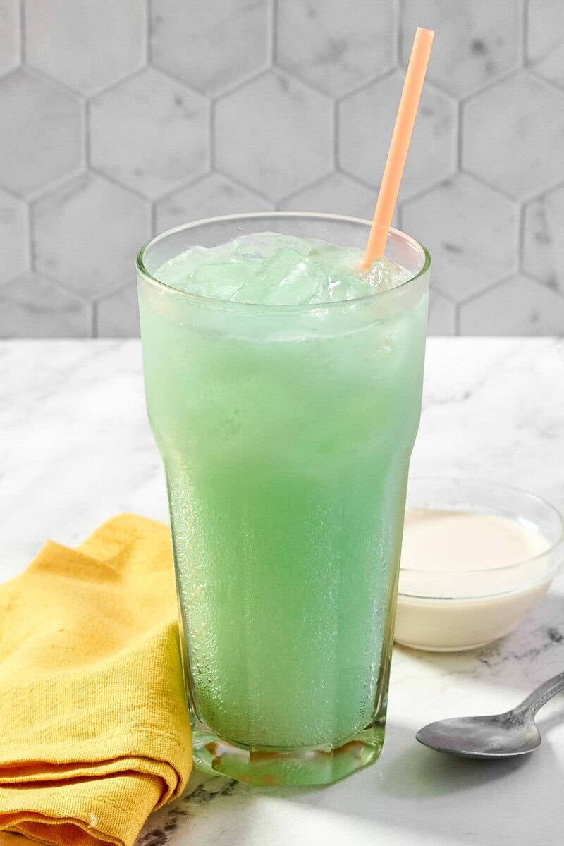 Vertical shot of a refreshing, creamy green Baja Blast soda with an orange straw and yellow napkin.