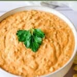 A bowl of creamy and cheesy taco dip garnished with a sprig of fresh cilantro.
