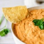 A bowl of creamy, cheesy taco dip with a tortilla chip pressed into it.