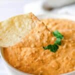 A tortilla chip that was dipped in taco dip held over the bowl of dip.