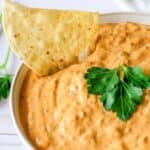 A bowl of creamy, cheesy taco dip with a tortilla chip in it.