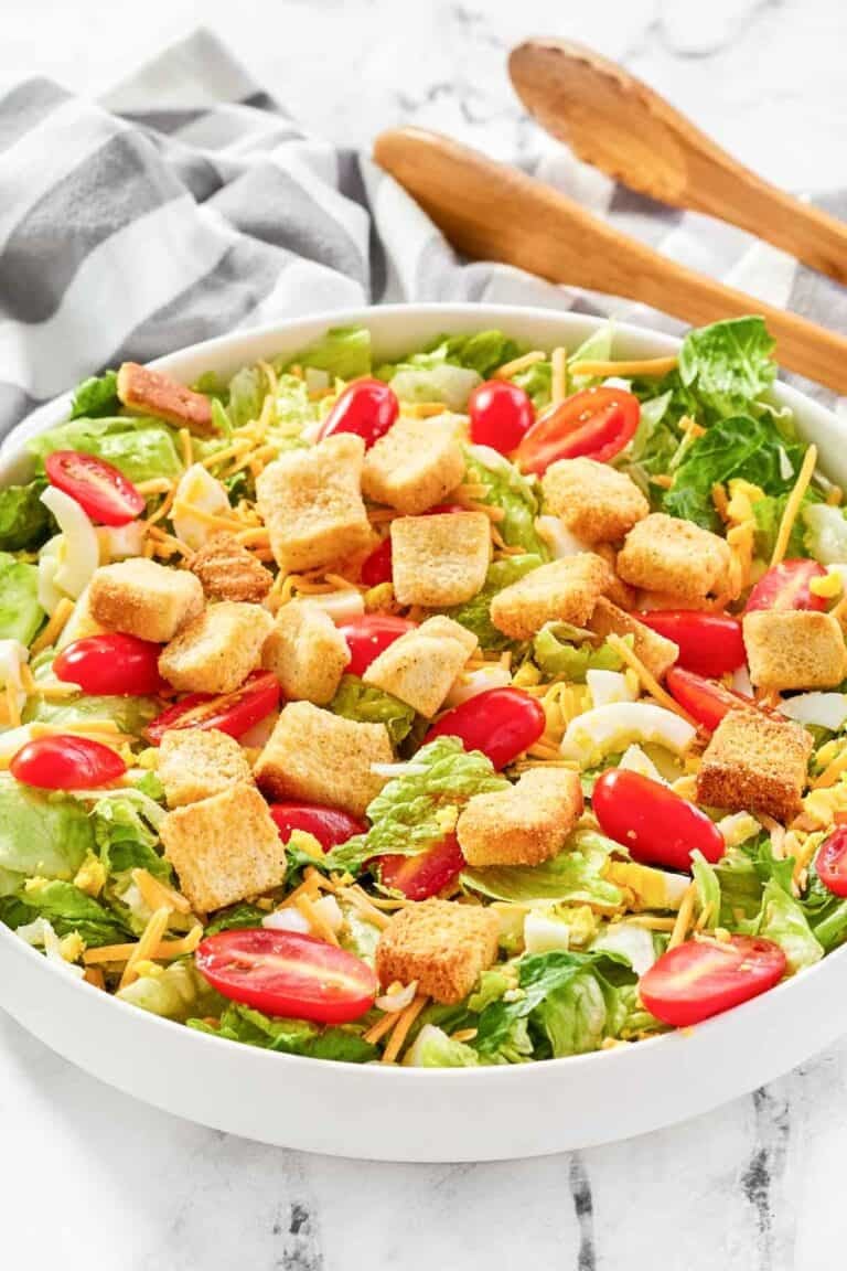 A bowl of copycat Texas Roadhouse house salad and salad tongs on a marble surface.