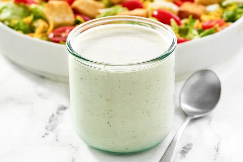 Copycat Texas Roadhouse ranch dressing in a glass jar and a salad behind it.