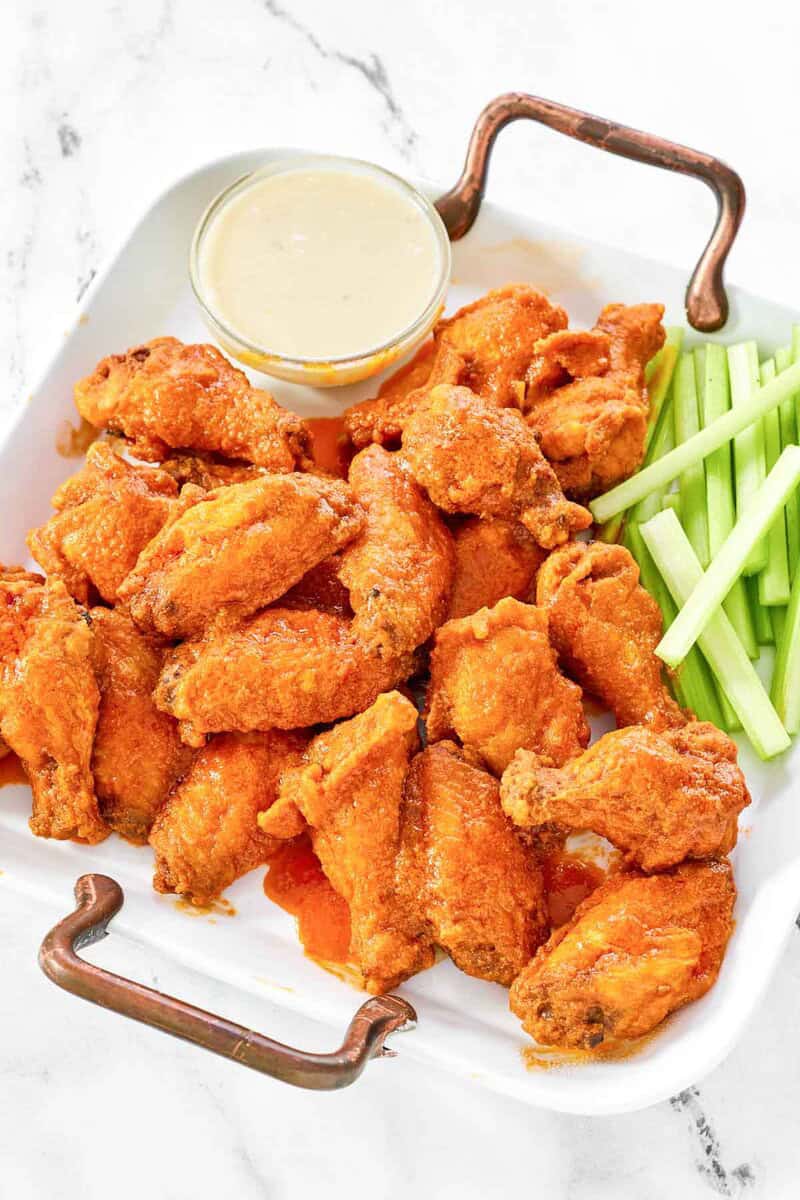 platter filled with crispy garlic Buffalo wings, served with celery sticks and a bowl of dipping sauce.