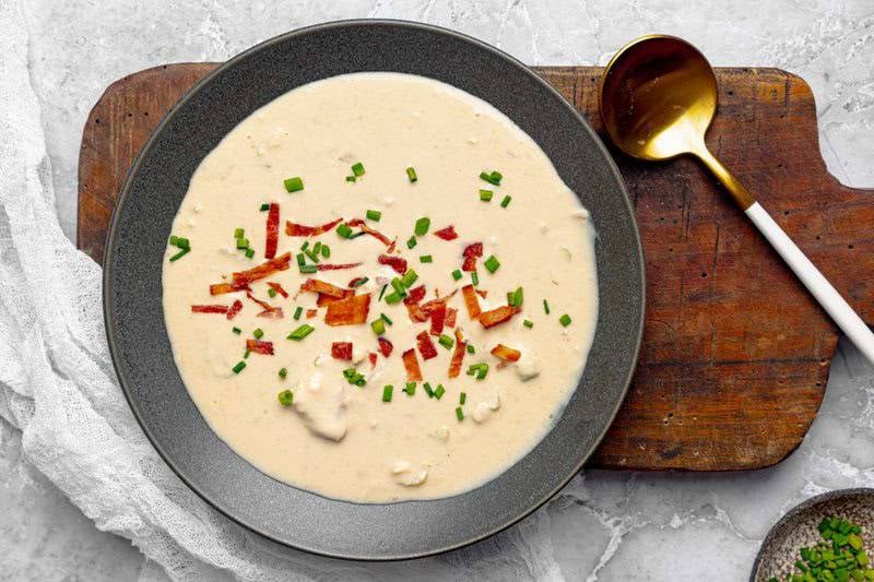 A bowl of creamy soup made with cheddar cheese, bacon, and beer on a rustic wood board.