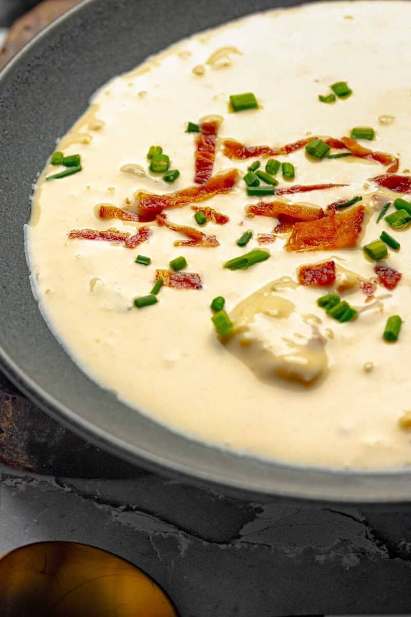 A bowl of beer cheese soup garnished with bacon bits and chives.