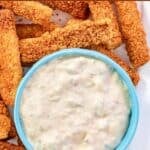 Crispy breaded fish sticks and a bowl of tartar sauce on a plate.