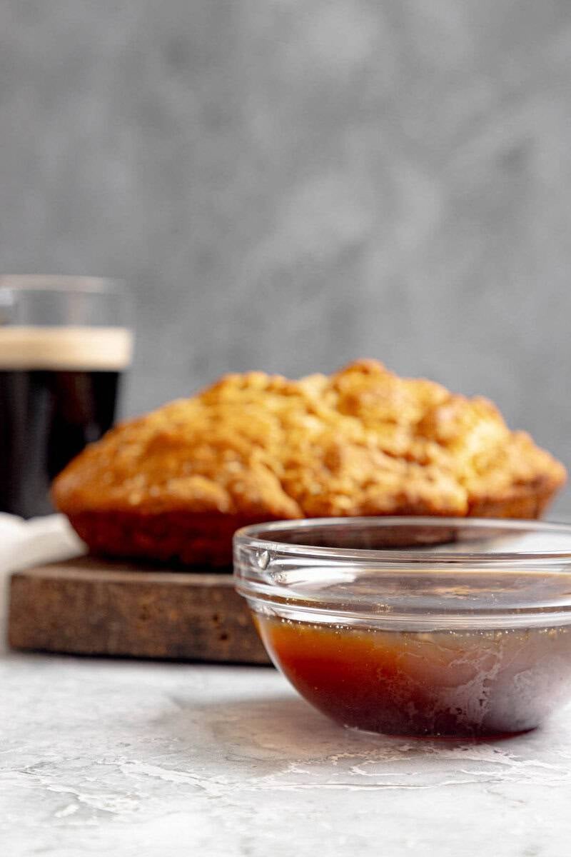 A bowl of sweet brown sugar Guinness stout sauce sits in front of a loaf of soda bread.