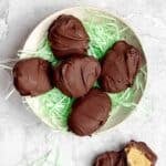 Candy peanut butter eggs on top of Easter basket straw on a plate.