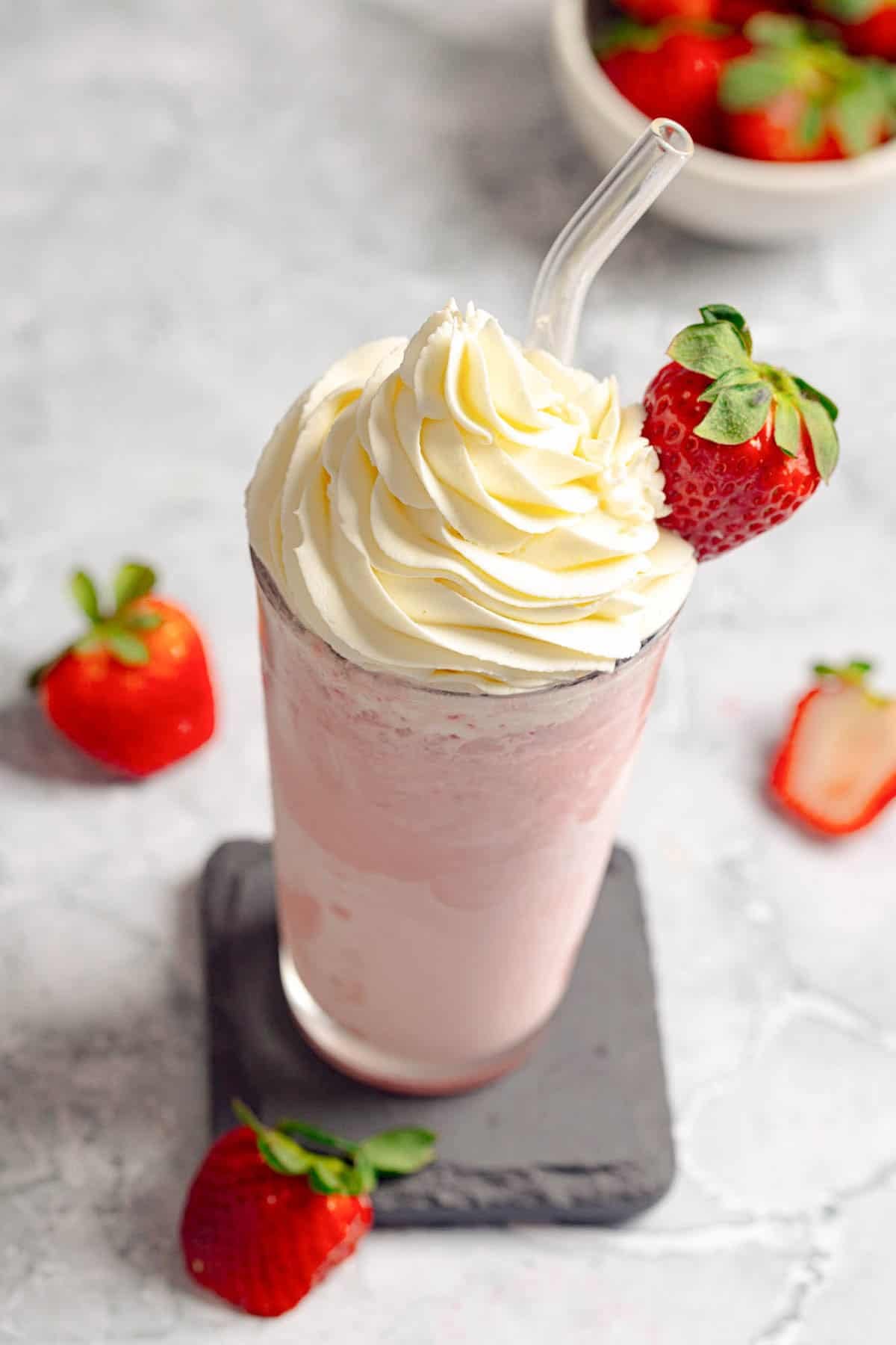 A creamy strawberry frappe and fresh strawberries around it.