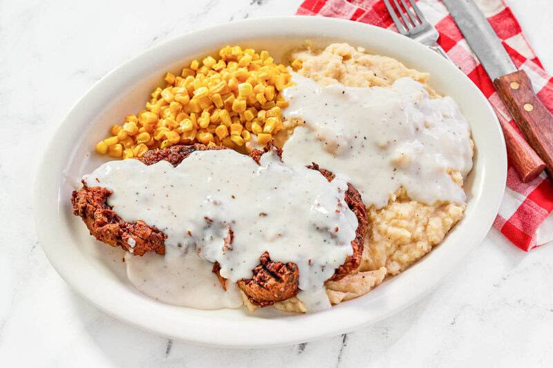White gravy covered chicken fried steak served with mashed potatoes and corn.