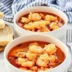 Shrimp in a buttery herb tomato broth in bowls served with bread.