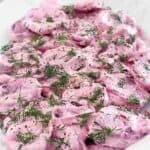 Roasted beet slices with sour cream sauce and fresh dill on a platter.