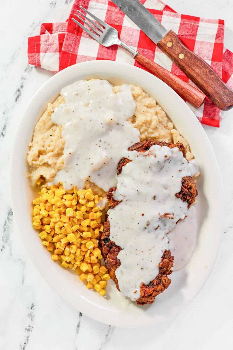 Country fried steak with creamy gravy, mashed potatoes, and corn on a plate.