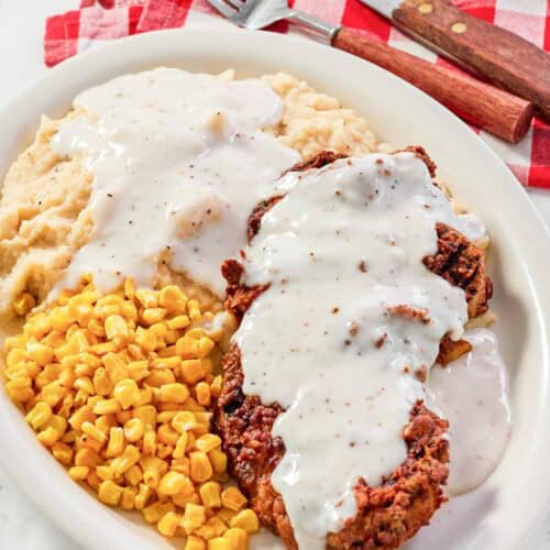 White gravy over chicken fried steak and mashed potatoes and corn on a plate.