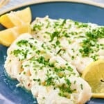 Lemon herb butter poached fish on a plate with lemon wedges.