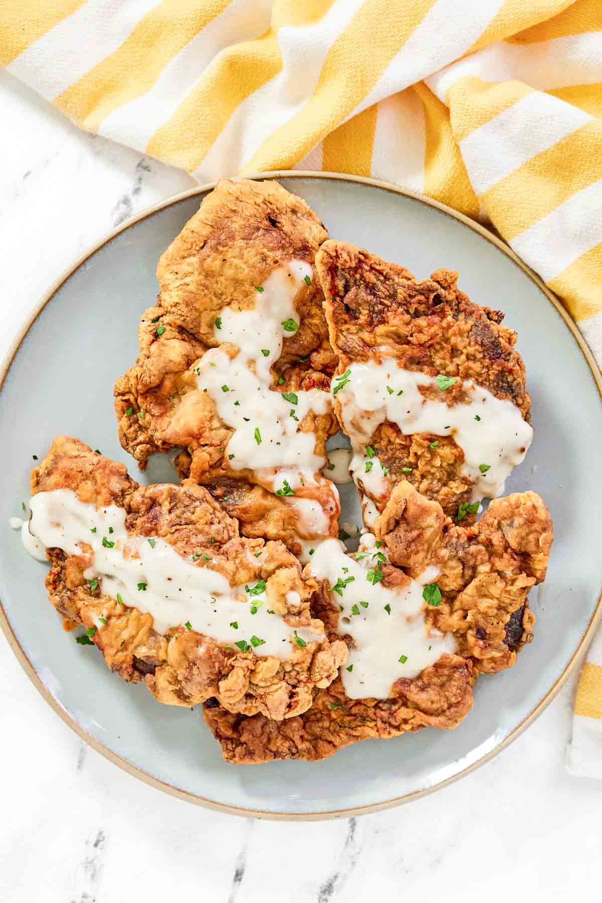 Crispy beer fried steaks topped with white gravy on a platter.