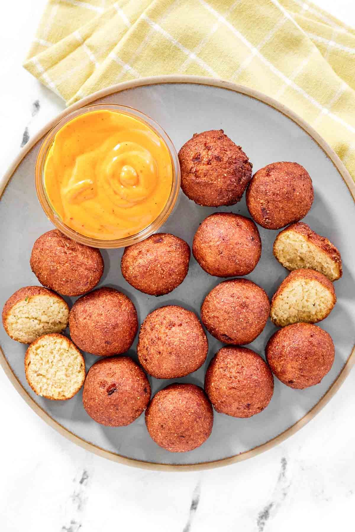 Fried cornbread balls and dipping sauce on a plate.