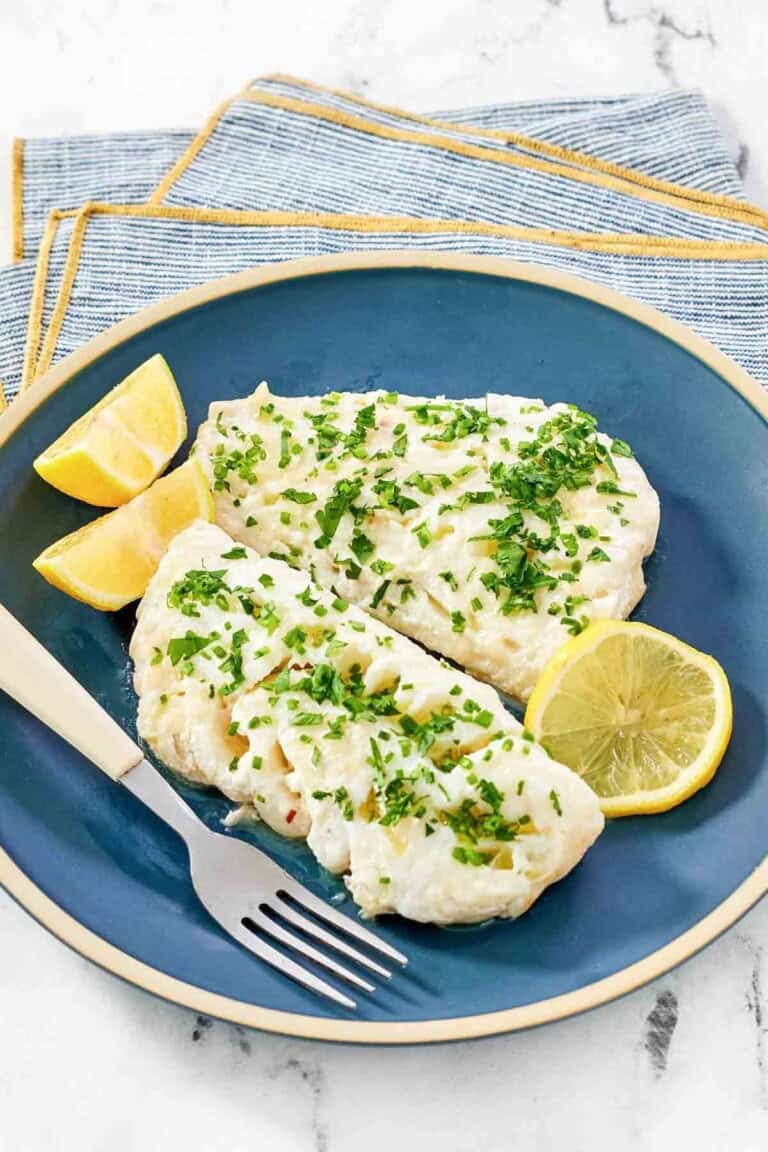 Lemony butter white fish and lemon wedges on a plate.