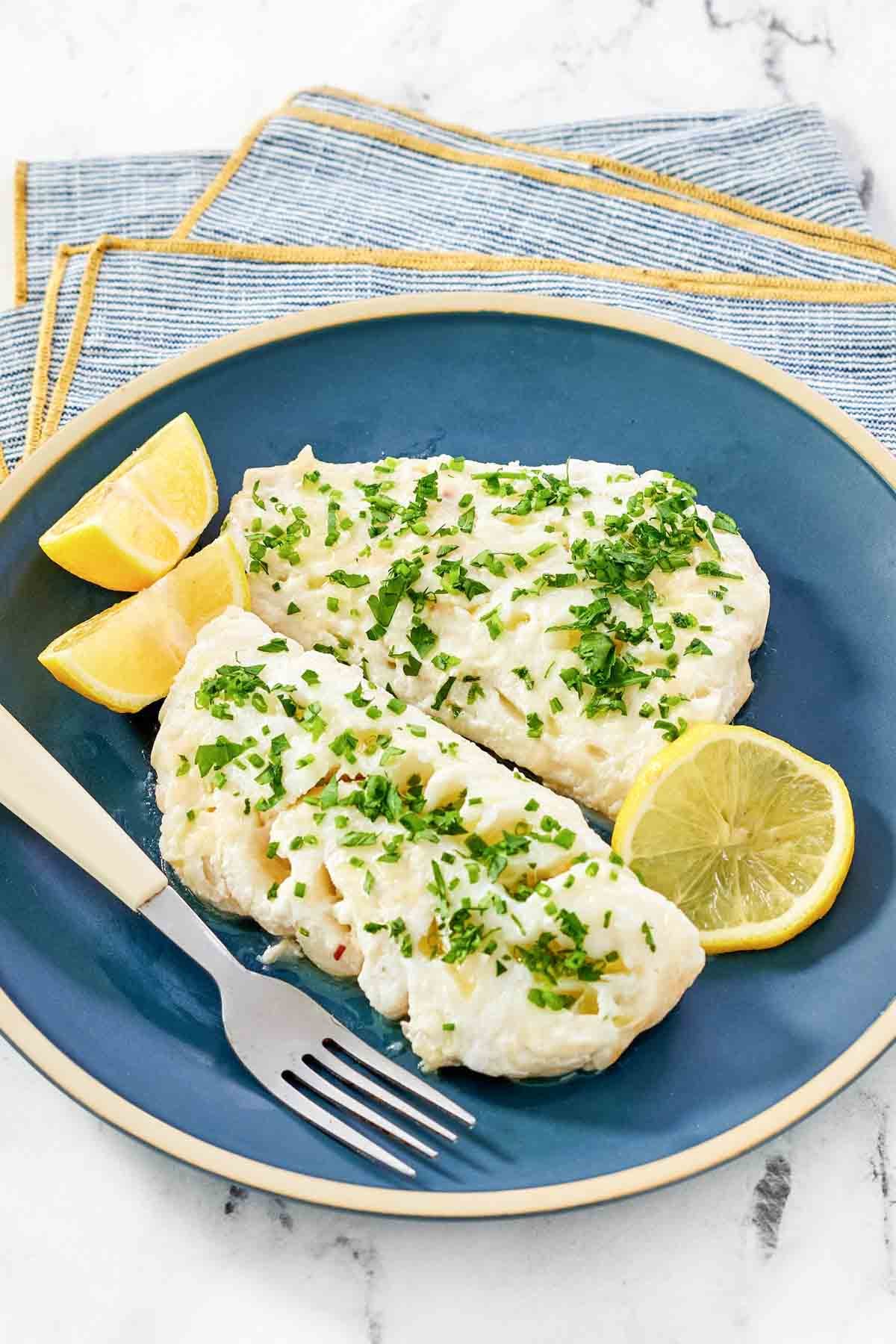 Lemony butter white fish and lemon wedges on a plate.