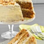 A slice of zucchini cake with cream cheese frosting on a plate in front of the cake.