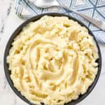 A bowl of buttery whipped potatoes with a spoon resting on a napkin beside it.