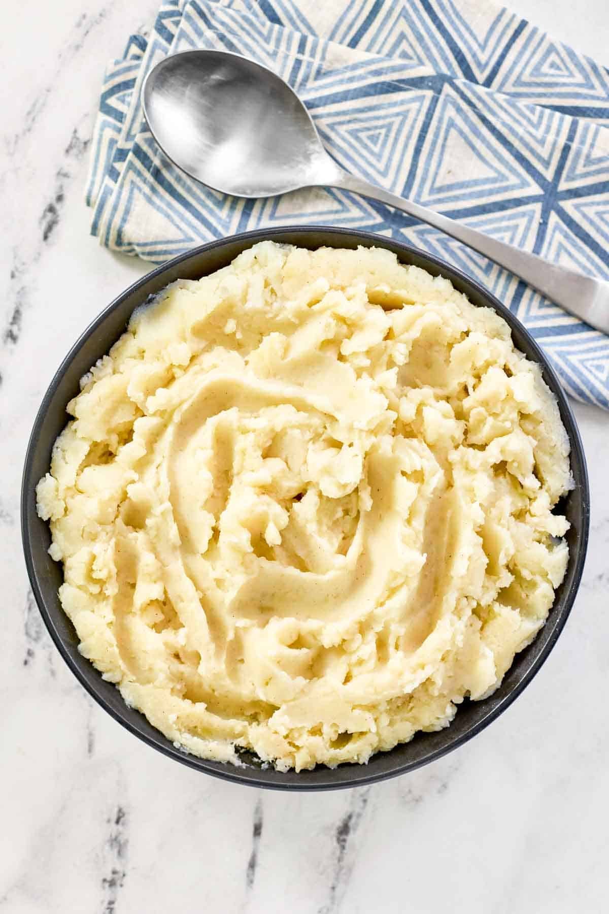 A bowl of buttery whipped potatoes with a spoon resting on a napkin beside it.