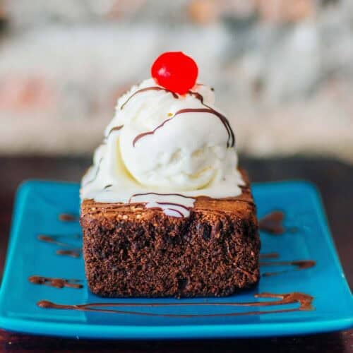 Chocolate brownie topped with ice cream, fudge sauce, and a cherry.