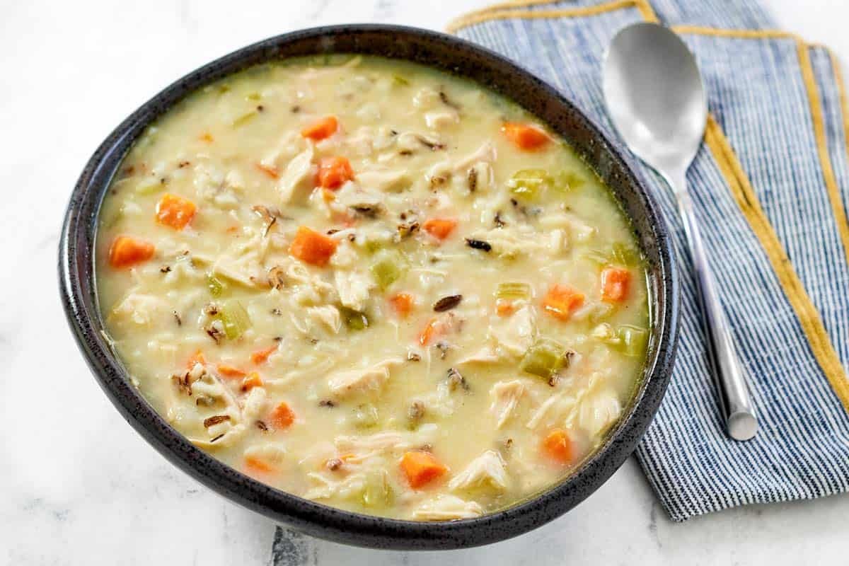 A bowl of hearty and creamy soup with chicken, veggies, and wild rice.