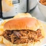 Slow cooker pulled pork sandwich and potato chips on a plate.