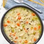 A bowl of thick and creamy soup with chicken, veggies, and wild rice.