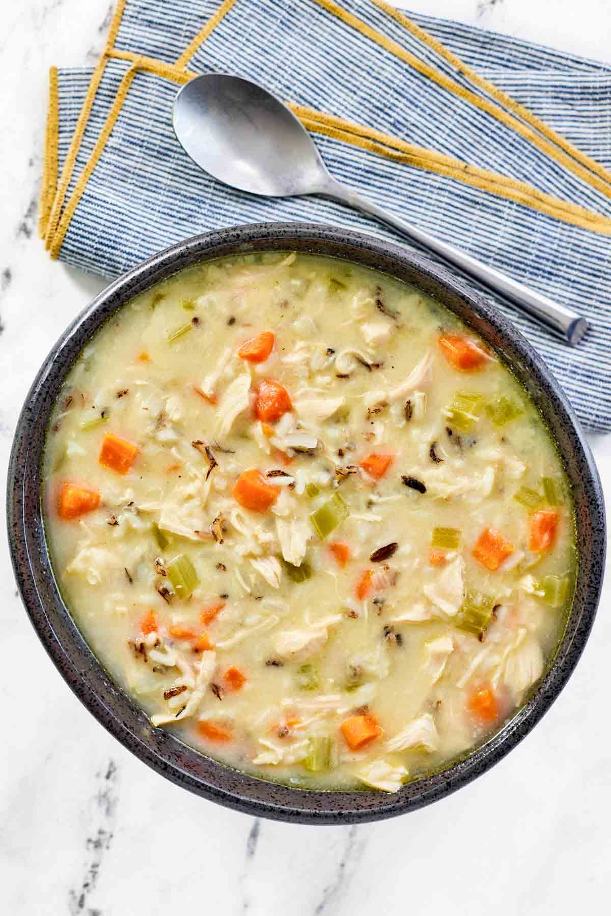 A bowl of thick and creamy soup with chicken, veggies, and wild rice.