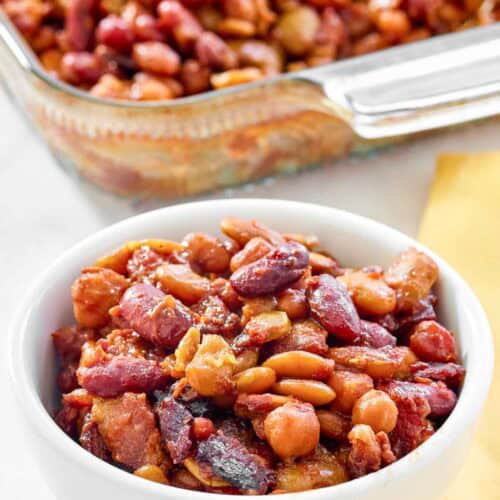 Five bean casserole with bacon in a bowl and glass baking dish.