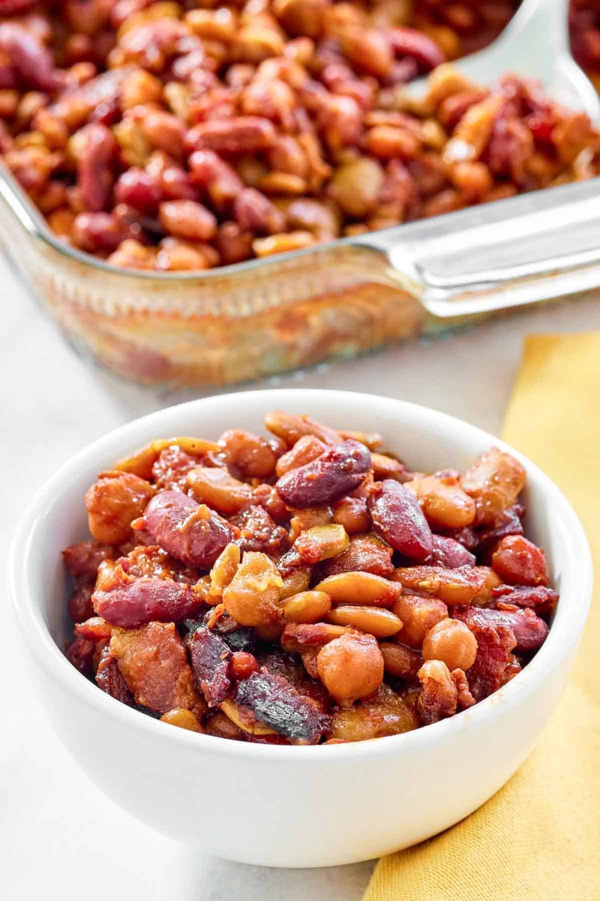 Five bean casserole with bacon in a bowl and glass baking dish.