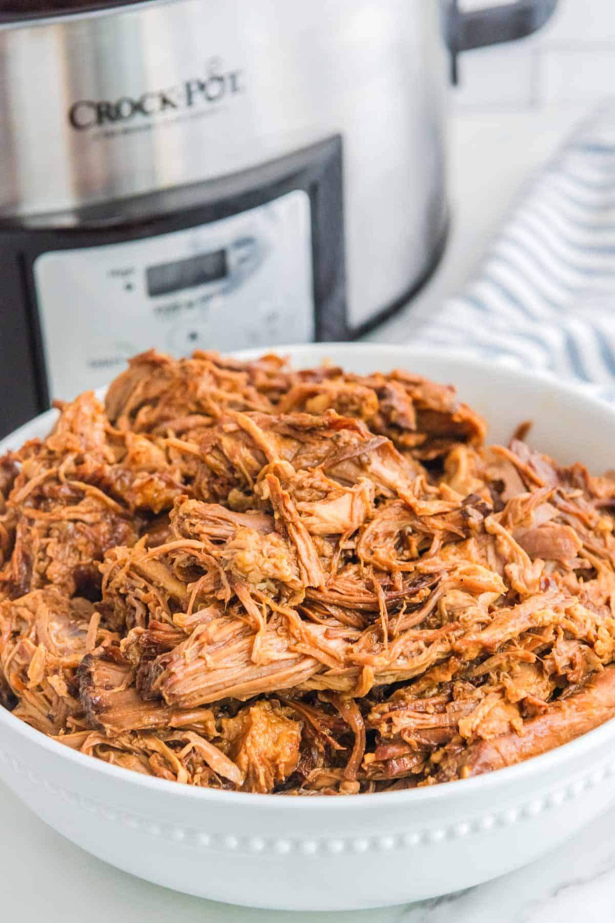 Shredded barbecue pork in a bowl and a Crock Pot behind it.