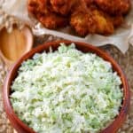 Homemade coleslaw in a bowl and a basket of chicken wings behind it.