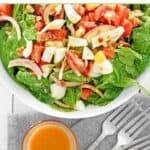 A bowl of spinach salad with hot bacon dressing and forks next to it.