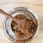 Homemade taco seasoning in a wooden measuring spoon held over a spice jar.