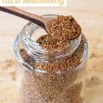 Homemade taco seasoning on a wooden measuring spoon on top of a small glass jar.