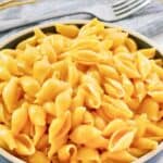 A bowl of copycat Velveeta shells and cheese and a fork on a napkin behind it.