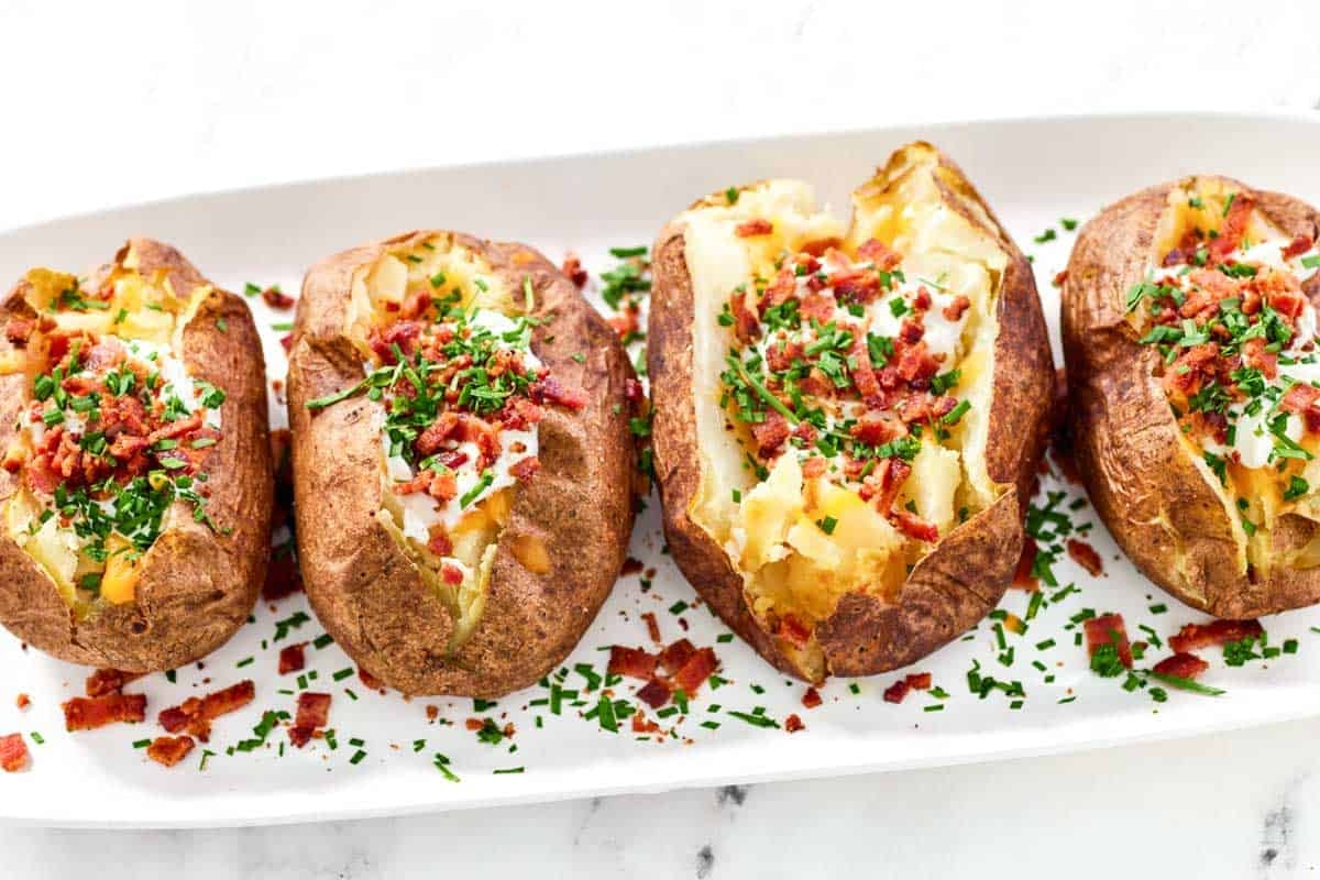 Baked potatoes topped with butter, cheese, bacon, sour cream, and chives.