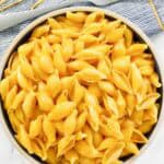 Cheesy shell pasta in a bowl and a fork on a napkin beside it.