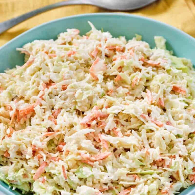 Creamy cabbage, carrot, onion, and pickle relish slaw in a bowl and a spoon resting on a napkin behind it.